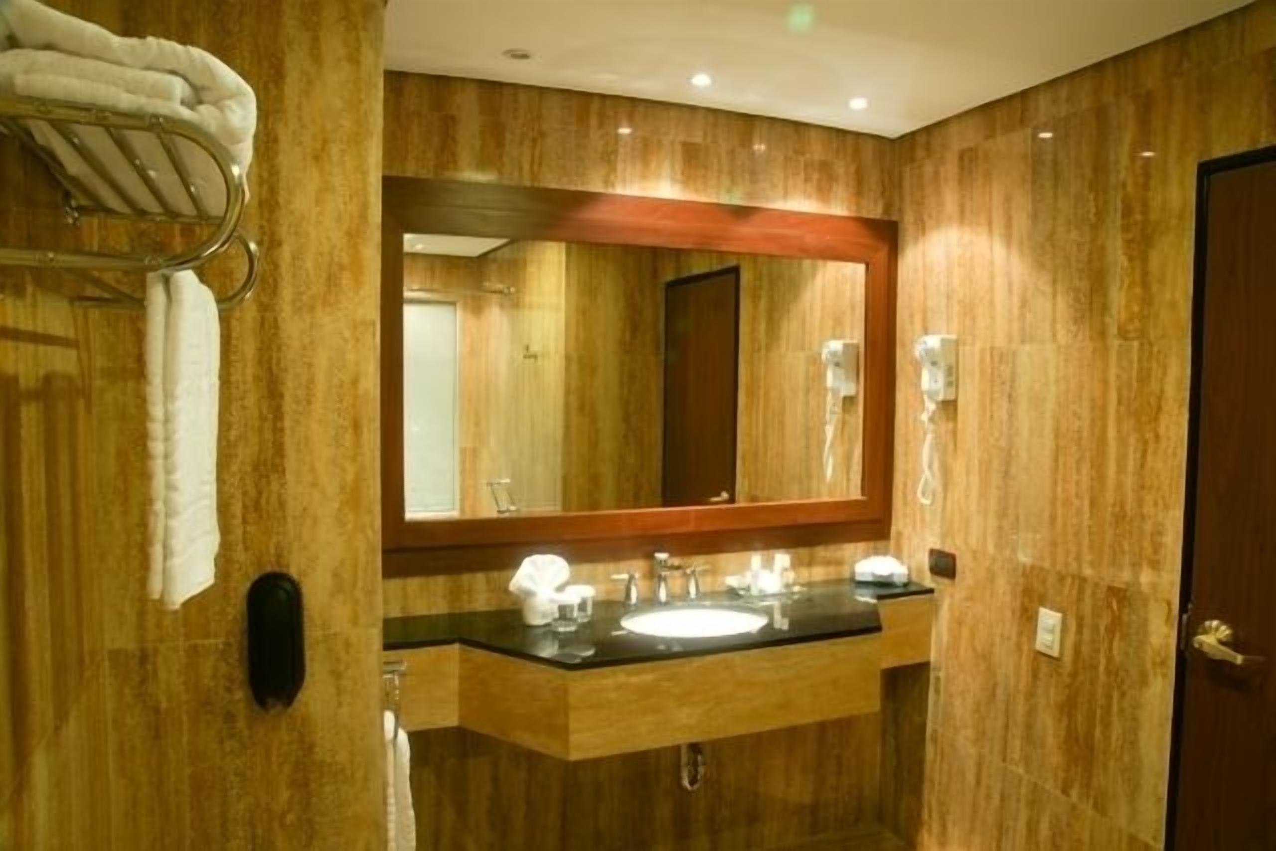 A bathroom with a wooden wall, a large mirror, a sink, and a towel rack.