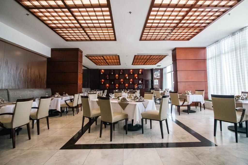 Un restaurante con varias mesas y sillas, una zona de bar central y un techo con diseño de cuadrícula.