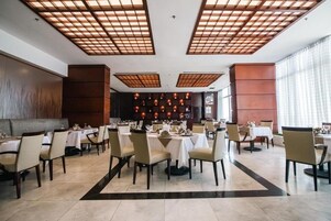 Un restaurante con varias mesas y sillas, una zona de bar central y un techo con diseño de cuadrícula.