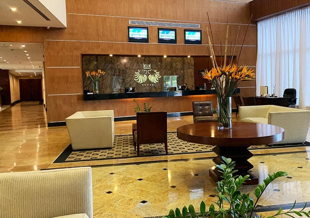 A hotel lobby with a reception desk, seating area, and a large vase with flowers.