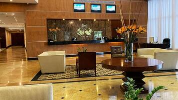 A hotel lobby with a reception desk, seating area, and a large vase with flowers.