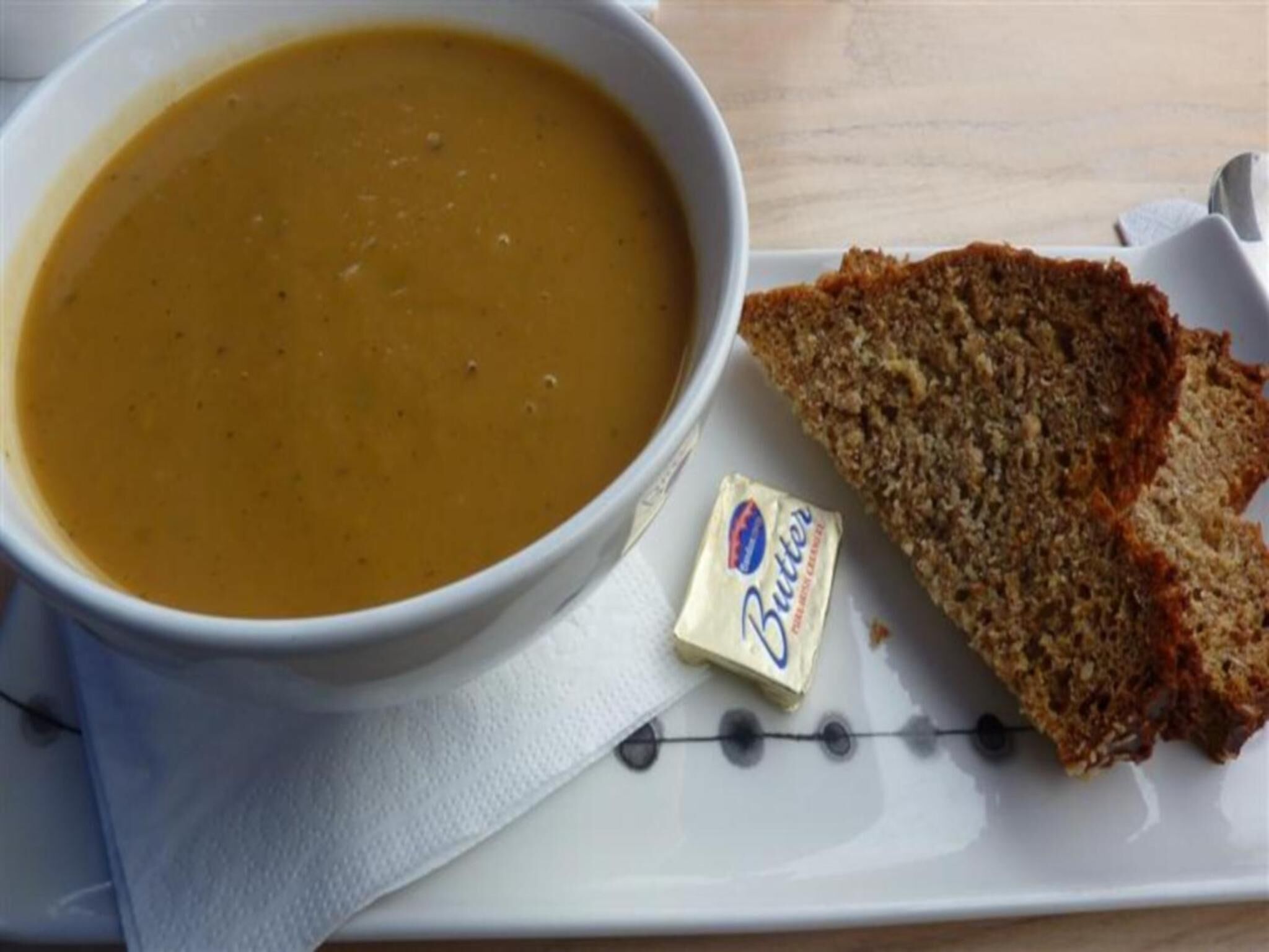 Un bol de soupe sur un plateau, accompagné de beurre et de deux tranches de pain.