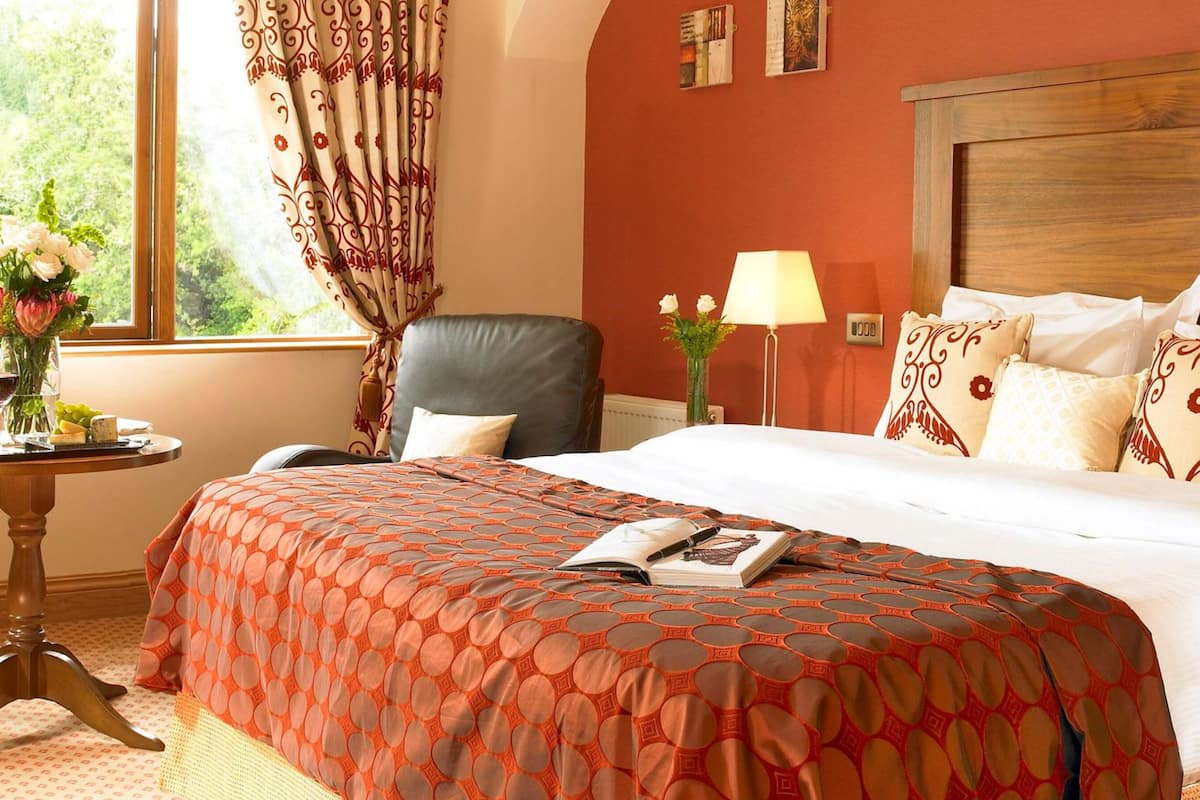 Una habitación de hotel con una cama grande, una silla, una mesa con un jarrón de flores y una ventana con cortinas.