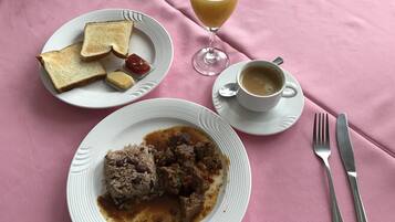 A breakfast setting with toast, butter, jam, a glass of orange juice, a cup of coffee, and a plate of meat and rice.