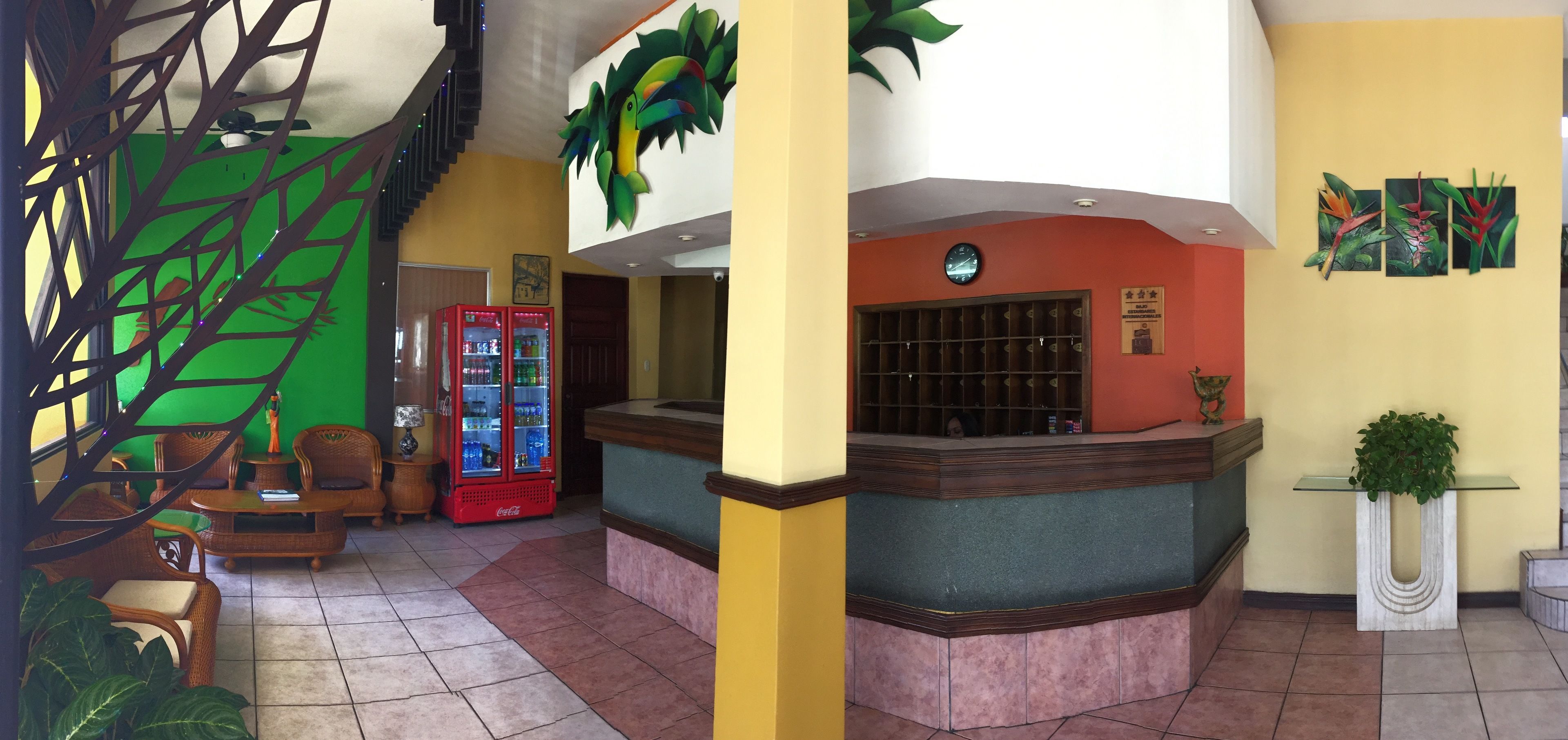 A reception area with a counter, seating, a Coca-Cola refrigerator, and tropical-themed wall art.