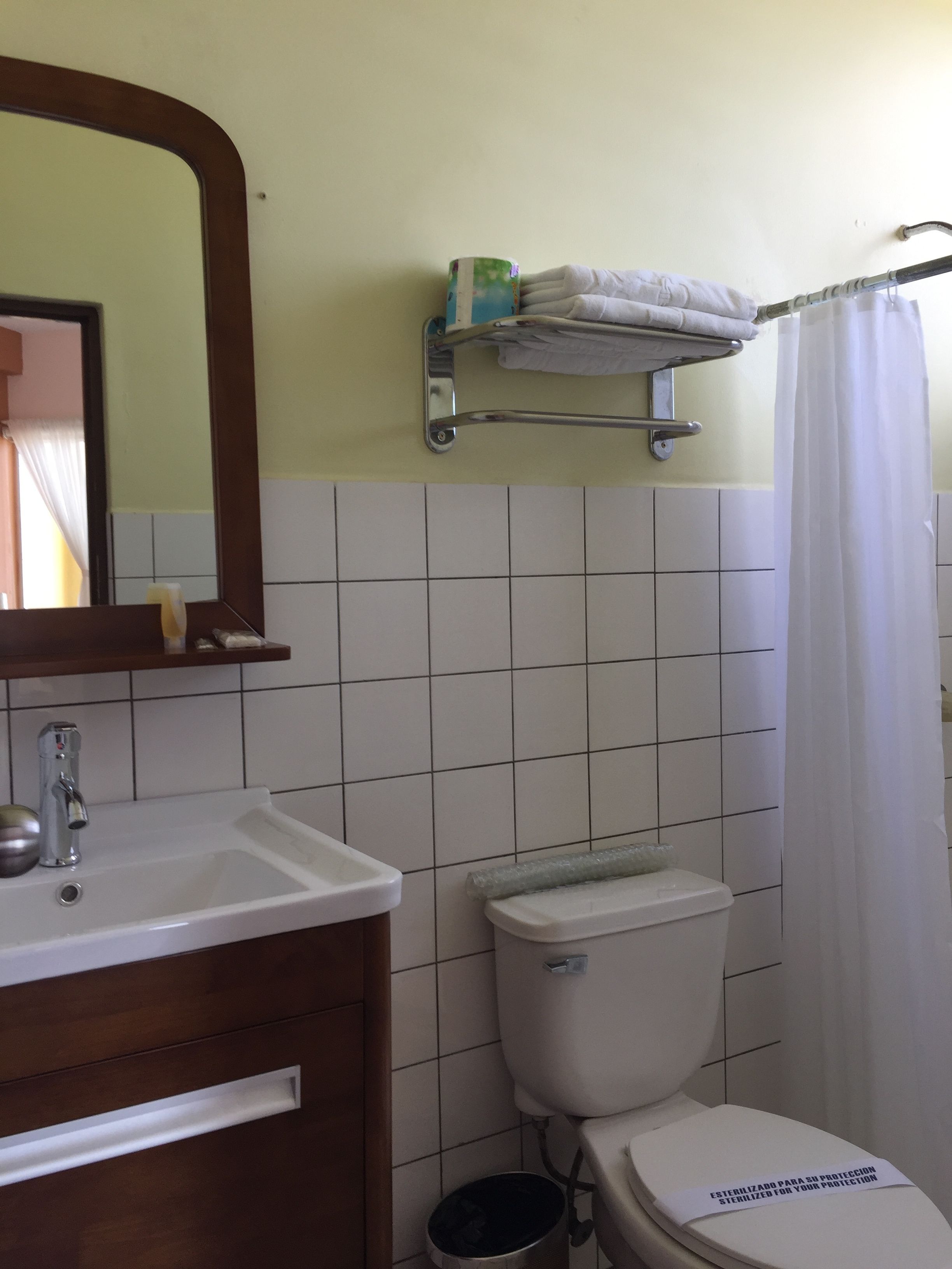 Un baño con lavamanos blanco, espejo, inodoro y cortina de ducha.