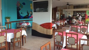 Un restaurant avec des tables et des chaises, une grande fresque murale et un téléviseur fixé au mur.