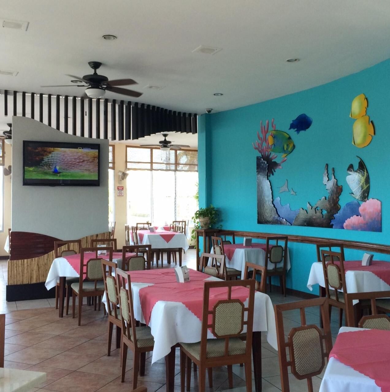 A restaurant with tables set for dining, a ceiling fan, and a mural on the wall.