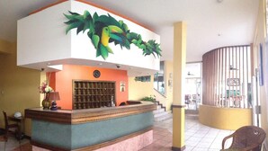 Un espace d’accueil agrémenté d’une grande fresque représentant un oiseau, d’une horloge et d’un comptoir orné d’une plante.