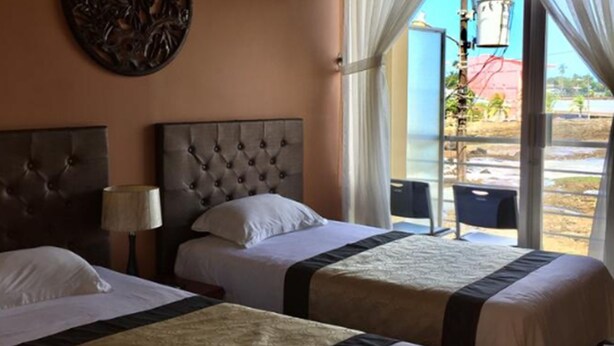 Une chambre d’hôtel avec deux lits, un ventilateur de plafond, un élément décoratif mural et une vue sur l’extérieur.