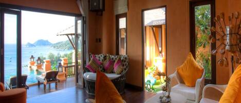 A room with a view of the sea, wicker furniture, and a small table with a lamp.