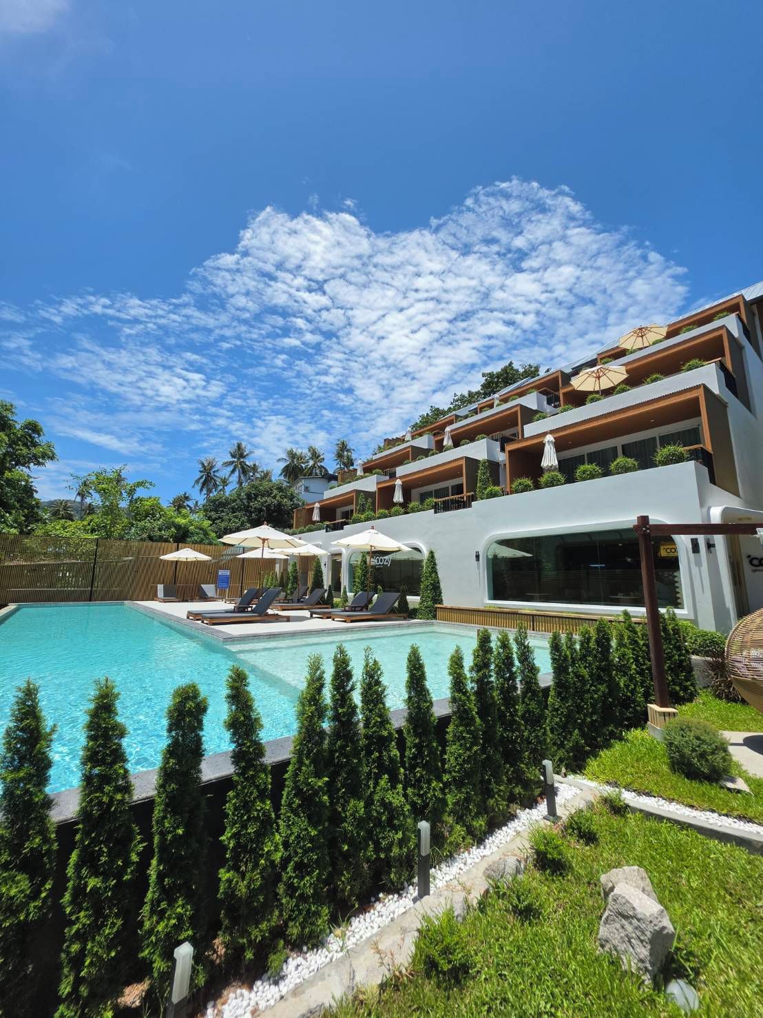 A modern hotel with a swimming pool, outdoor seating, and a view of the sky.