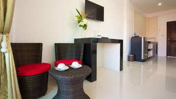 A modern hotel room with wicker furniture, a flat-screen TV, a small table with cups, and a kitchen area.