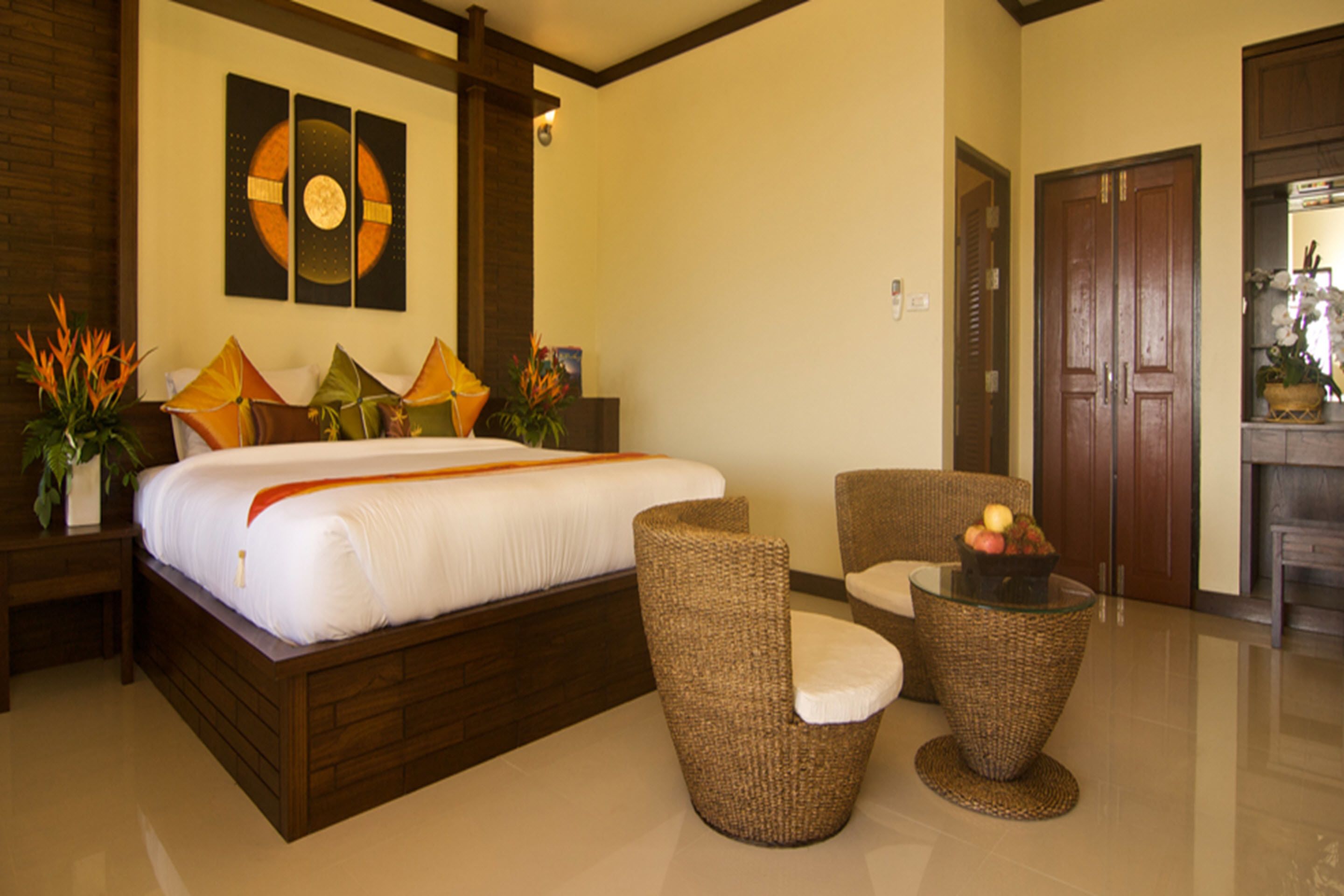 Habitación de hotel con una cama grande, dos sillas, una mesita con fruta y una pared decorada con arte abstracto.