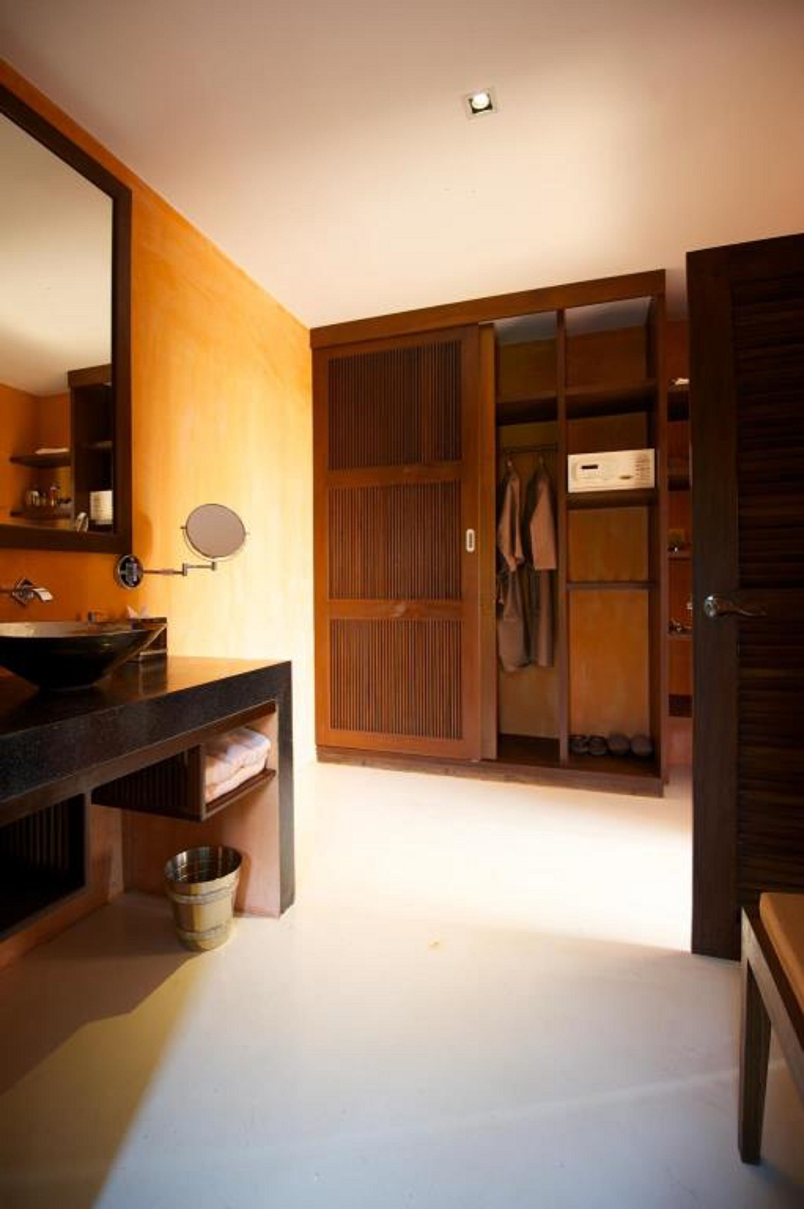 A modern bathroom with a wooden vanity, a large mirror, and a walk-in closet with sliding doors.