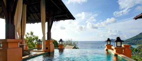 An infinity pool with a view of the ocean, surrounded by a wooden pavilion and lanterns.