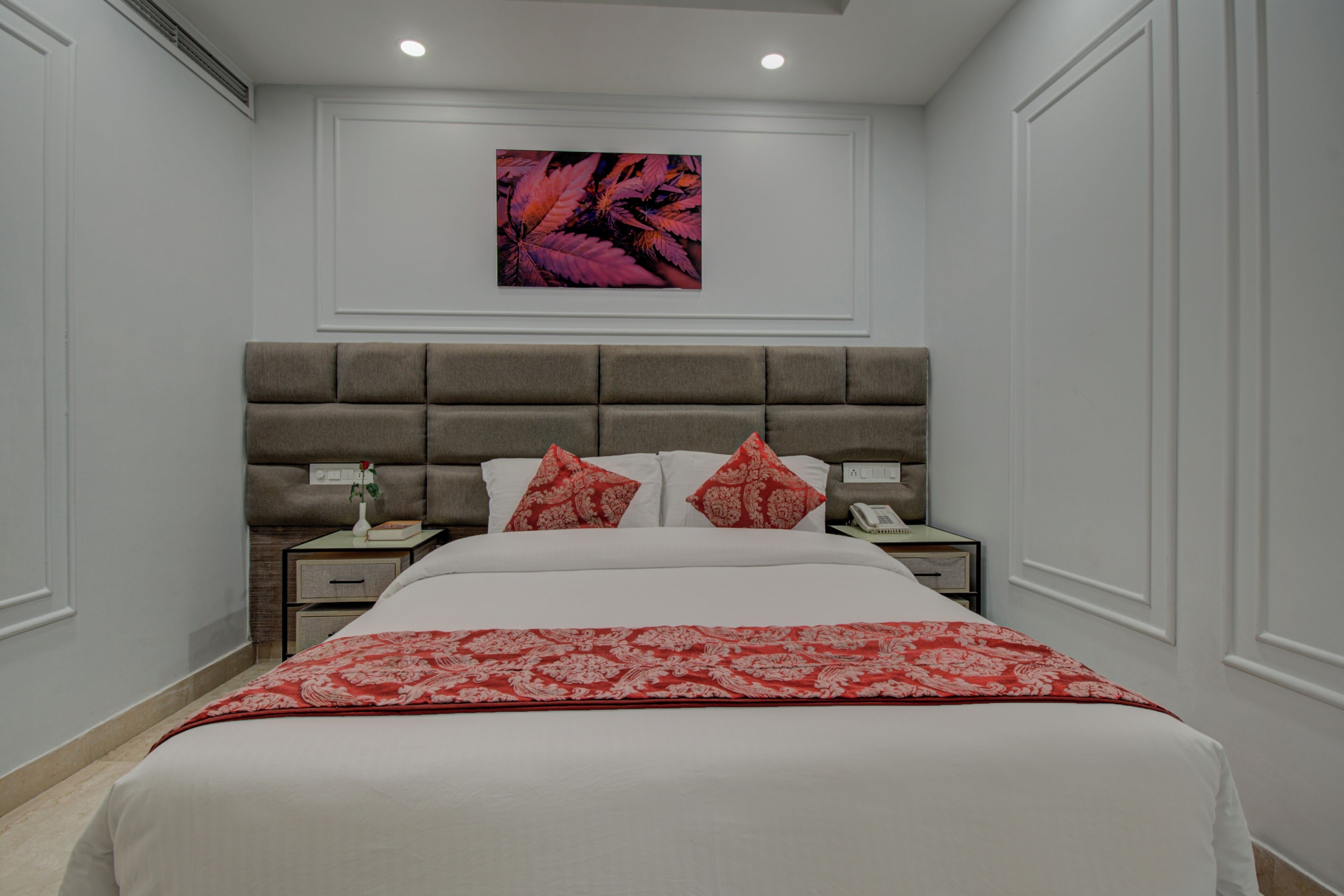 A bedroom with a large bed, a headboard, two bedside tables, a nightstand, and a wall-mounted artwork.