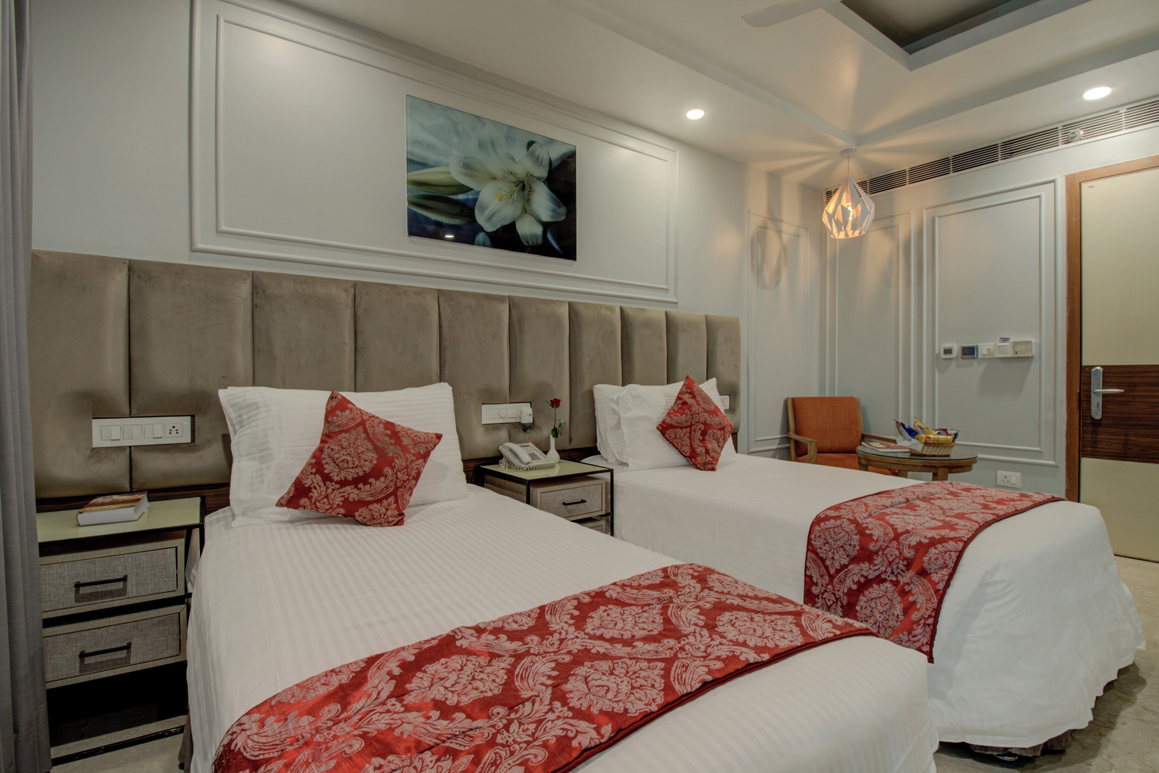 A hotel room with two beds, a large mirror, a painting, a chandelier, and a small table with a basket.
