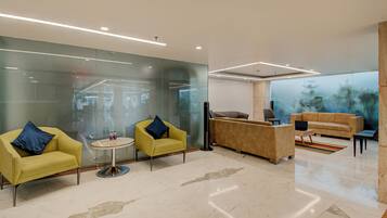 A modern lobby with glass walls, a reception desk, yellow armchairs, a sofa, and a laptop on a table.