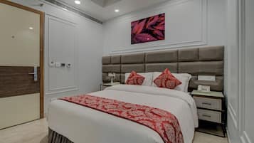 A modern bedroom with a large bed, a headboard with storage, bedside tables, and a wall-mounted artwork.