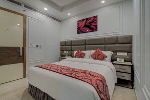 A modern bedroom with a large bed, a headboard with storage, bedside tables, and a wall-mounted artwork.