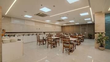 Un'ampia sala da pranzo con numerosi tavoli e sedie, un banco buffet con varie pietanze, e un moderno design del soffitto con illuminazione a incasso.