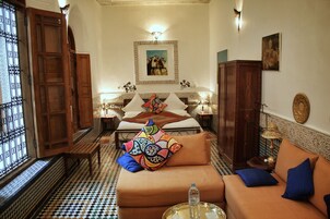 Quarto com piso xadrez, sofá com almofadas coloridas, cama com cabeceira estampada e um quadro na parede.