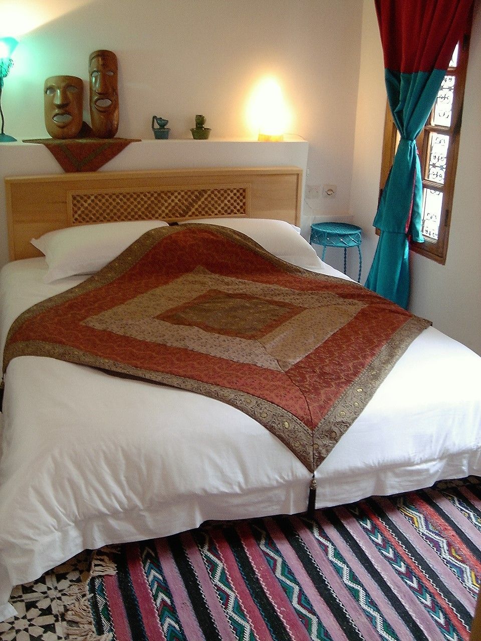 A bed with a patterned bedspread, a headboard, and a nightstand with a lamp.