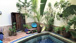 A pool area with a tiled edge, potted plants, and outdoor furniture.