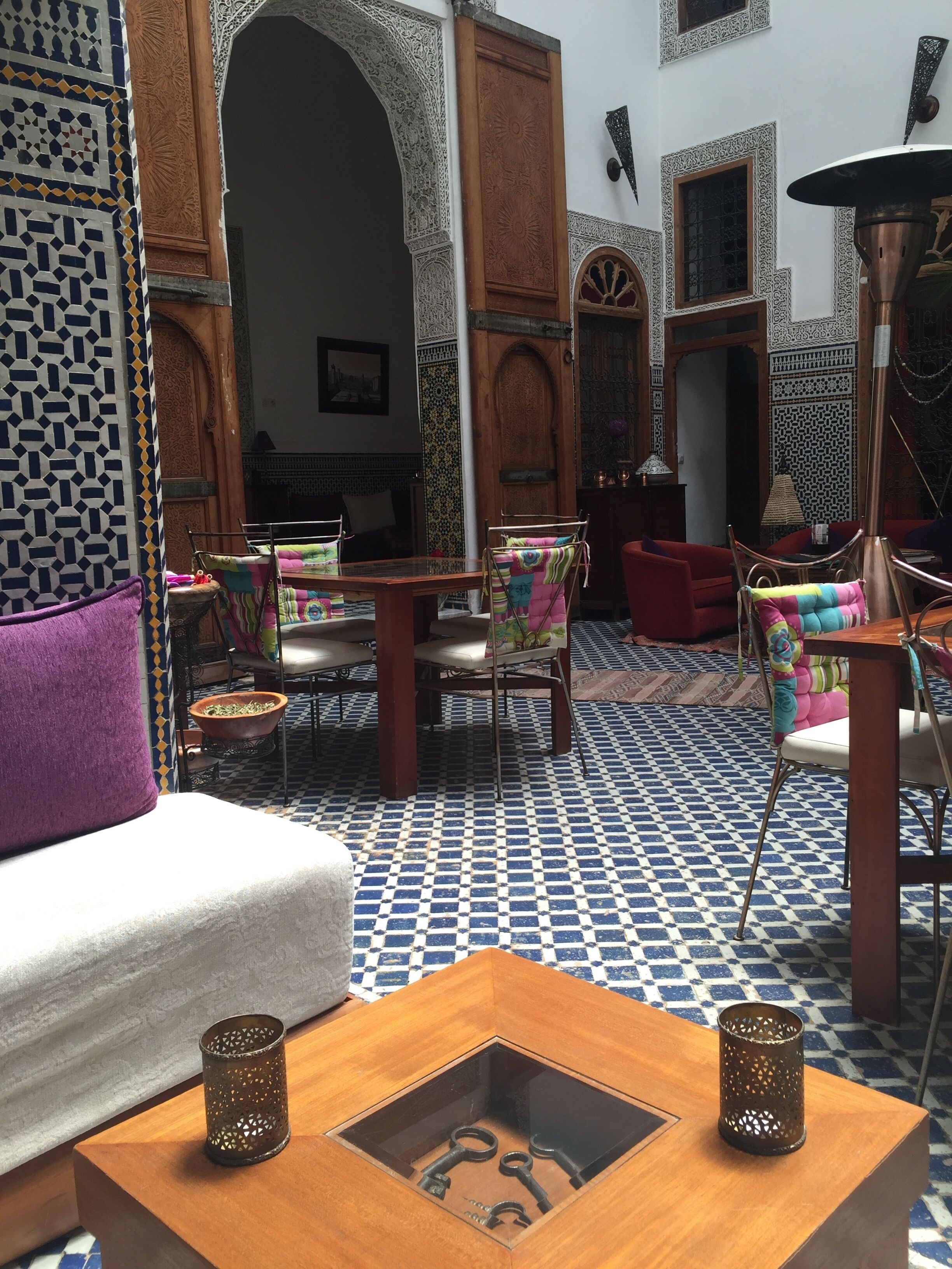 A traditional Moroccan interior with a patterned tile floor, a wooden coffee table with a glass top, and a sofa with a purple cushion.