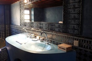 A bathroom with a large, curved sink, a decorative mirror, and patterned tile walls.