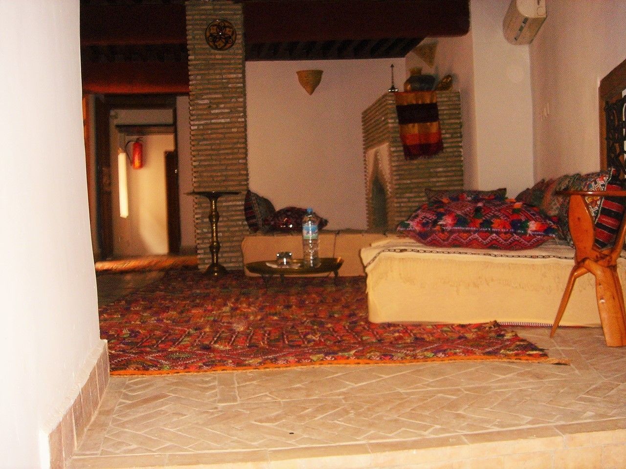 A living room with a patterned rug, a sofa, a small table with a water bottle, and a chair.