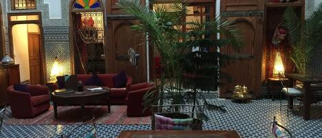 A traditional Moroccan interior with a seating area, a dining table, and decorative elements.