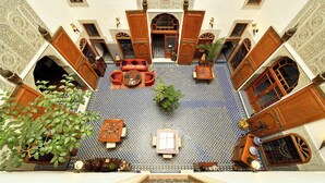 A courtyard with a central seating area, surrounded by wooden doors and arches, and a tiled floor.