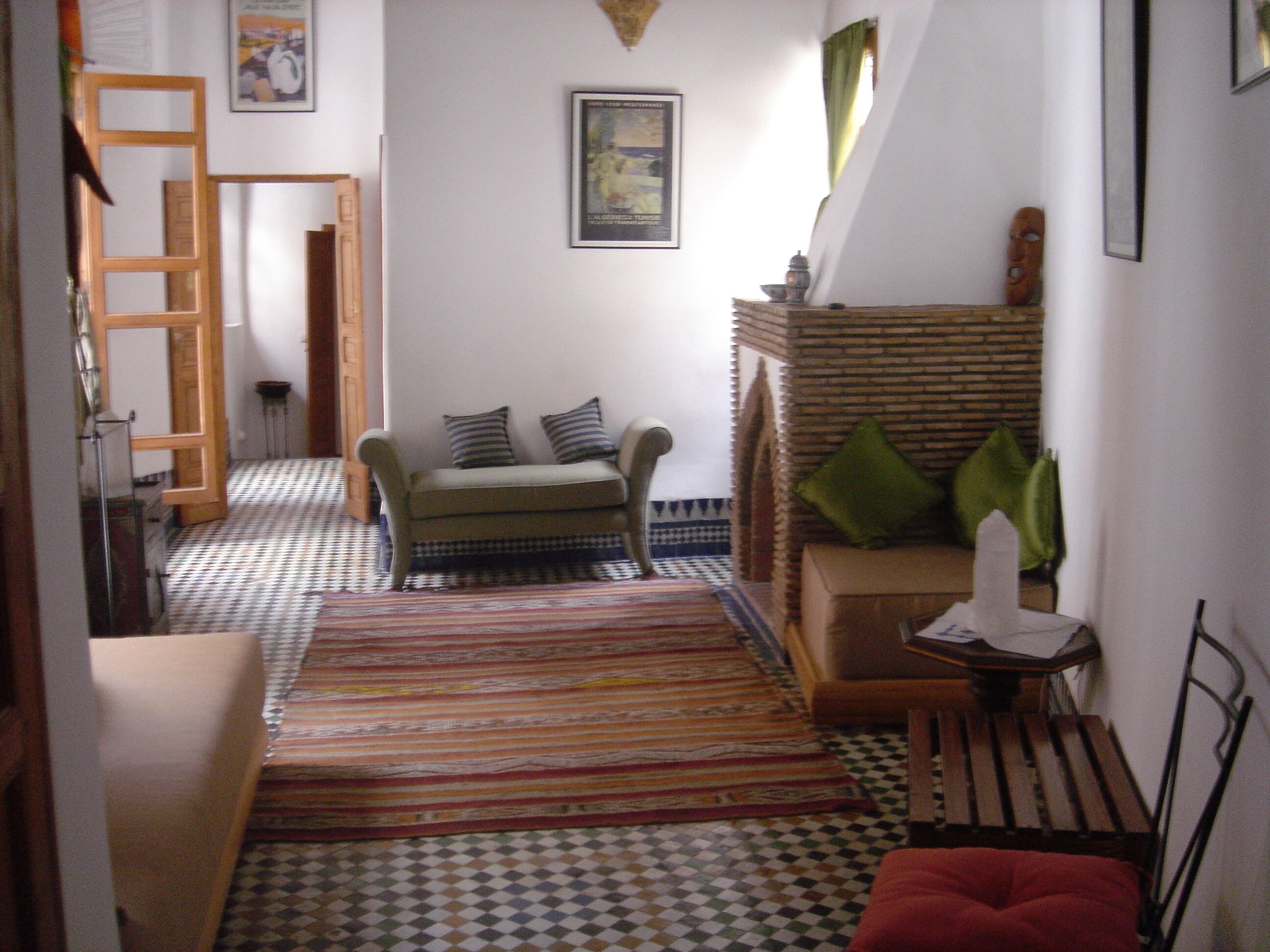 Un couloir étroit avec un sol à motifs, un canapé avec des coussins, une petite table avec une bougie et une échelle en bois appuyée contre le mur.