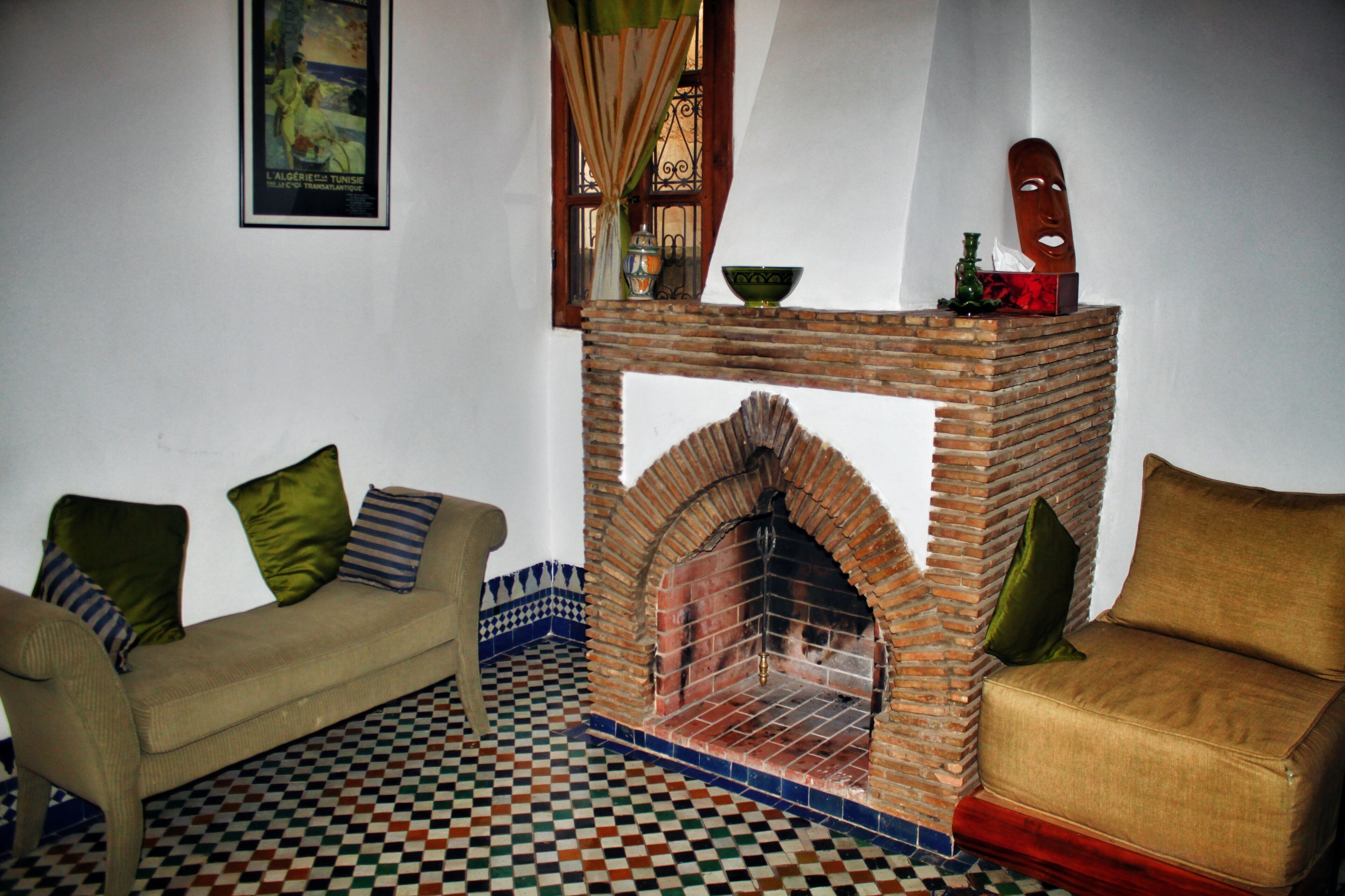 A room with a checkered floor, a brick fireplace, a sofa, and a poster on the wall.