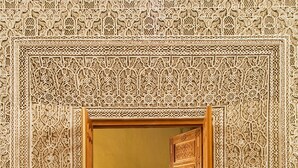 An ornate doorway with intricate tile work, leading to a room with a patterned floor and a potted plant.