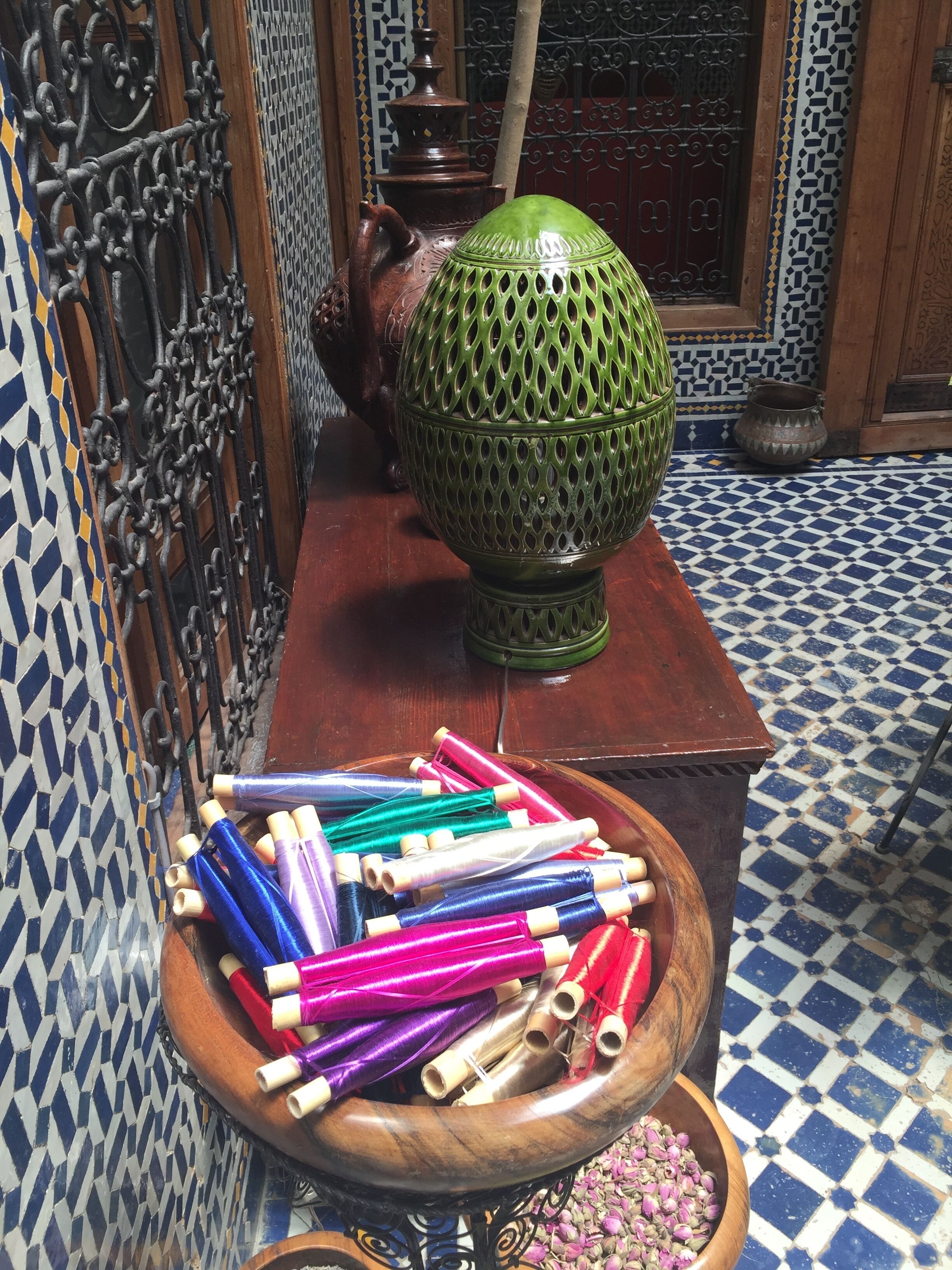 A room with a tiled floor, a wooden table with a green decorative bowl, and a bowl of colorful yarn.