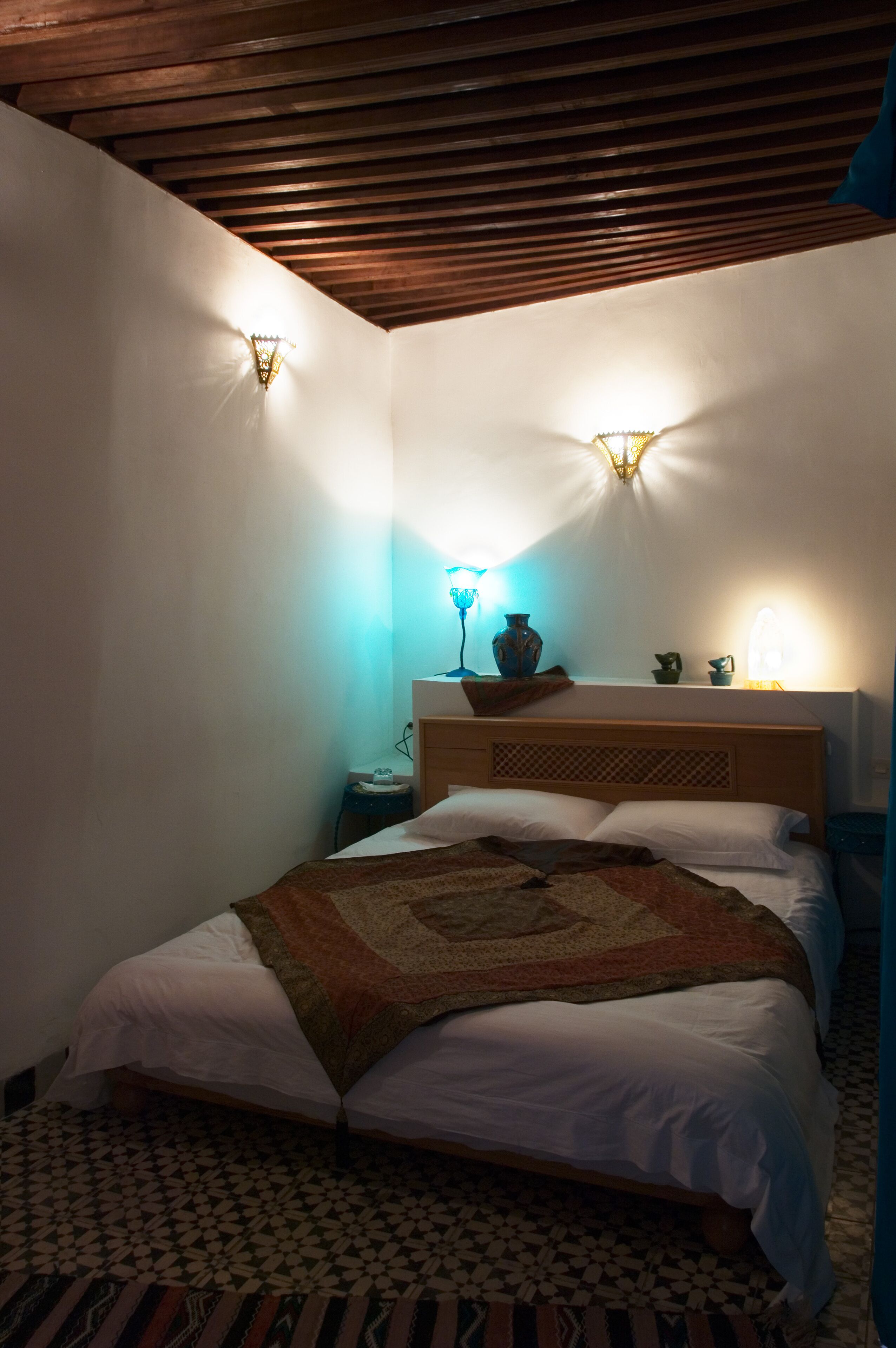 Une chambre à coucher comprenant un lit, une table de chevet, une lampe fixée au mur et un vase décoratif.