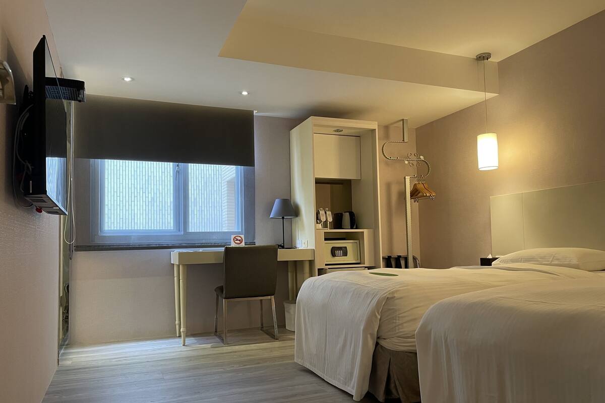 Une chambre d’hôtel équipée d’un lit, d’un bureau, d’une chaise, d’une armoire, d’une télévision et d’une fenêtre.
