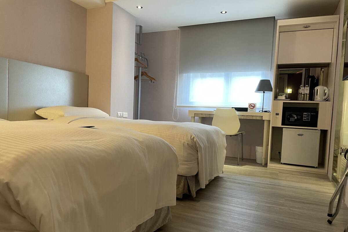 Une chambre d’hôtel avec deux lits, un bureau, une chaise, une armoire et une kitchenette.