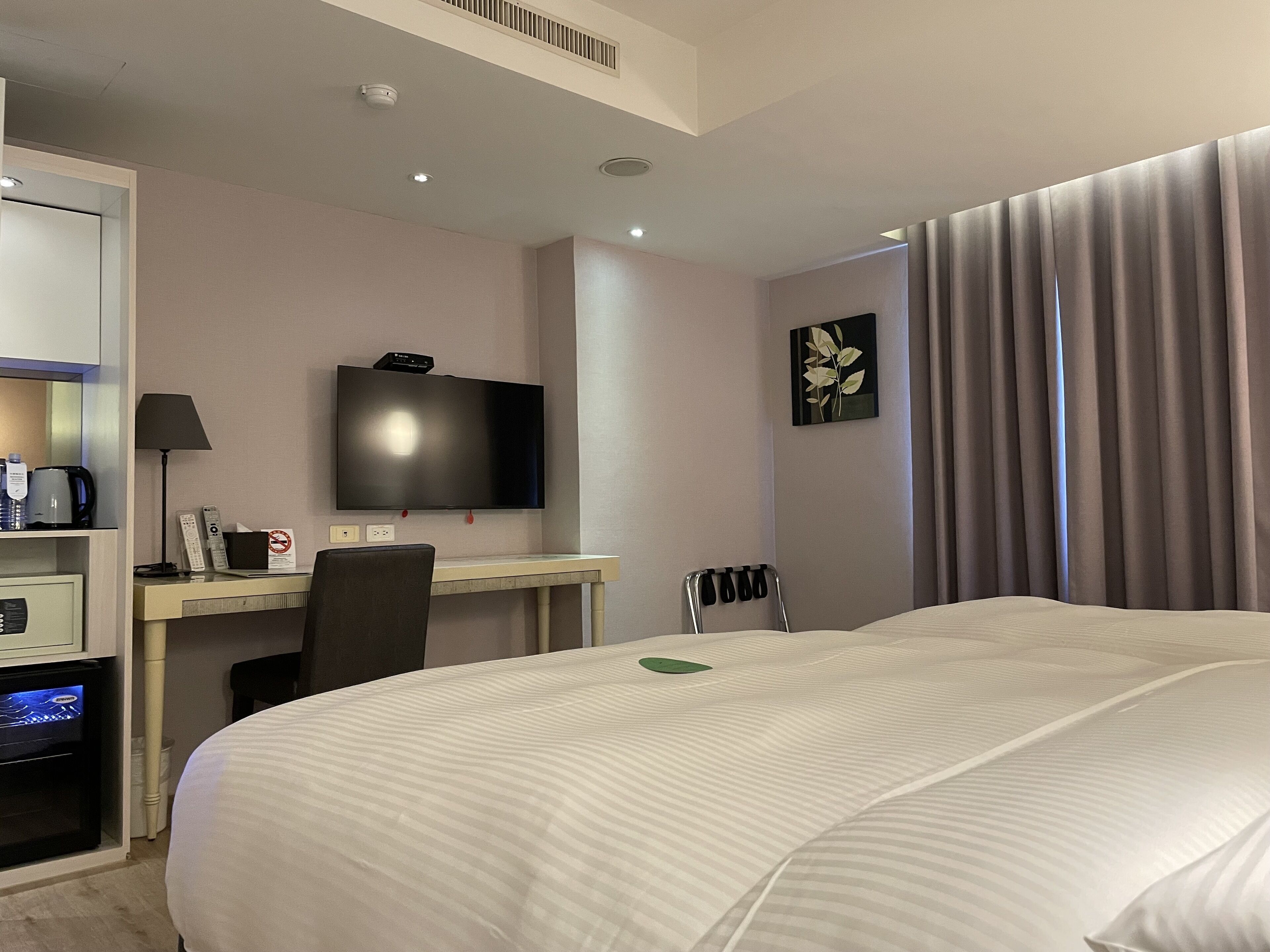 Habitación de hotel con cama, escritorio con televisor de pantalla plana, silla, cafetera y un mueble pequeño.