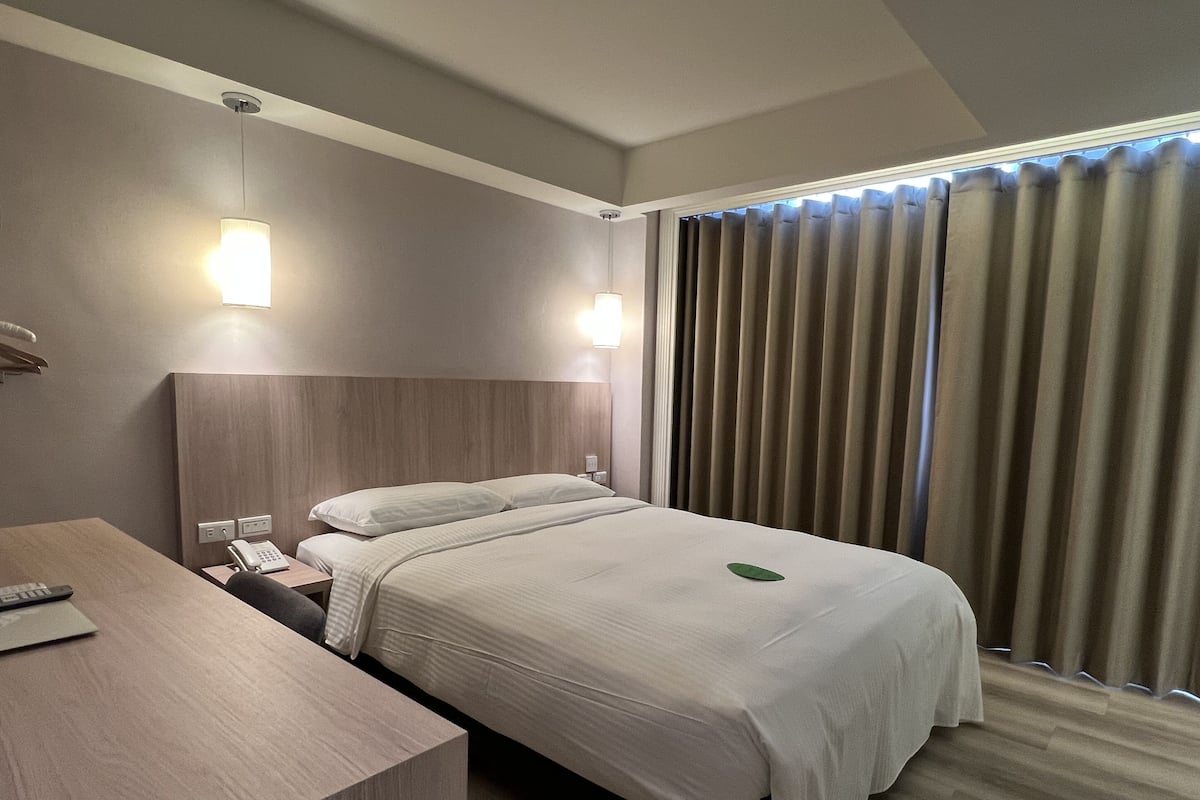 Une chambre d’hôtel avec un lit, une table de chevet, une lampe et des rideaux.