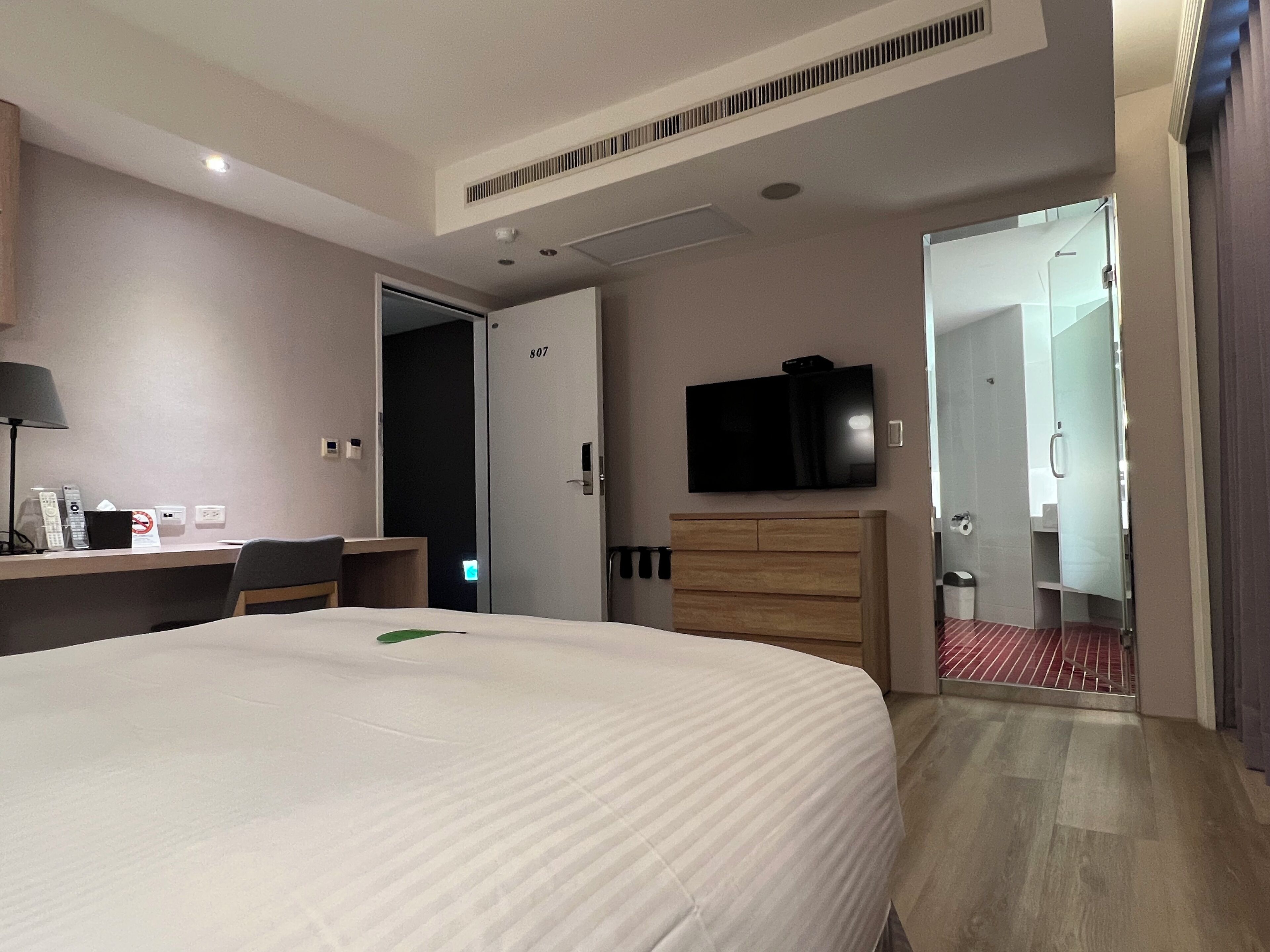 A hotel room with a bed, a desk, a television, a wardrobe, and a bathroom visible through an open door.