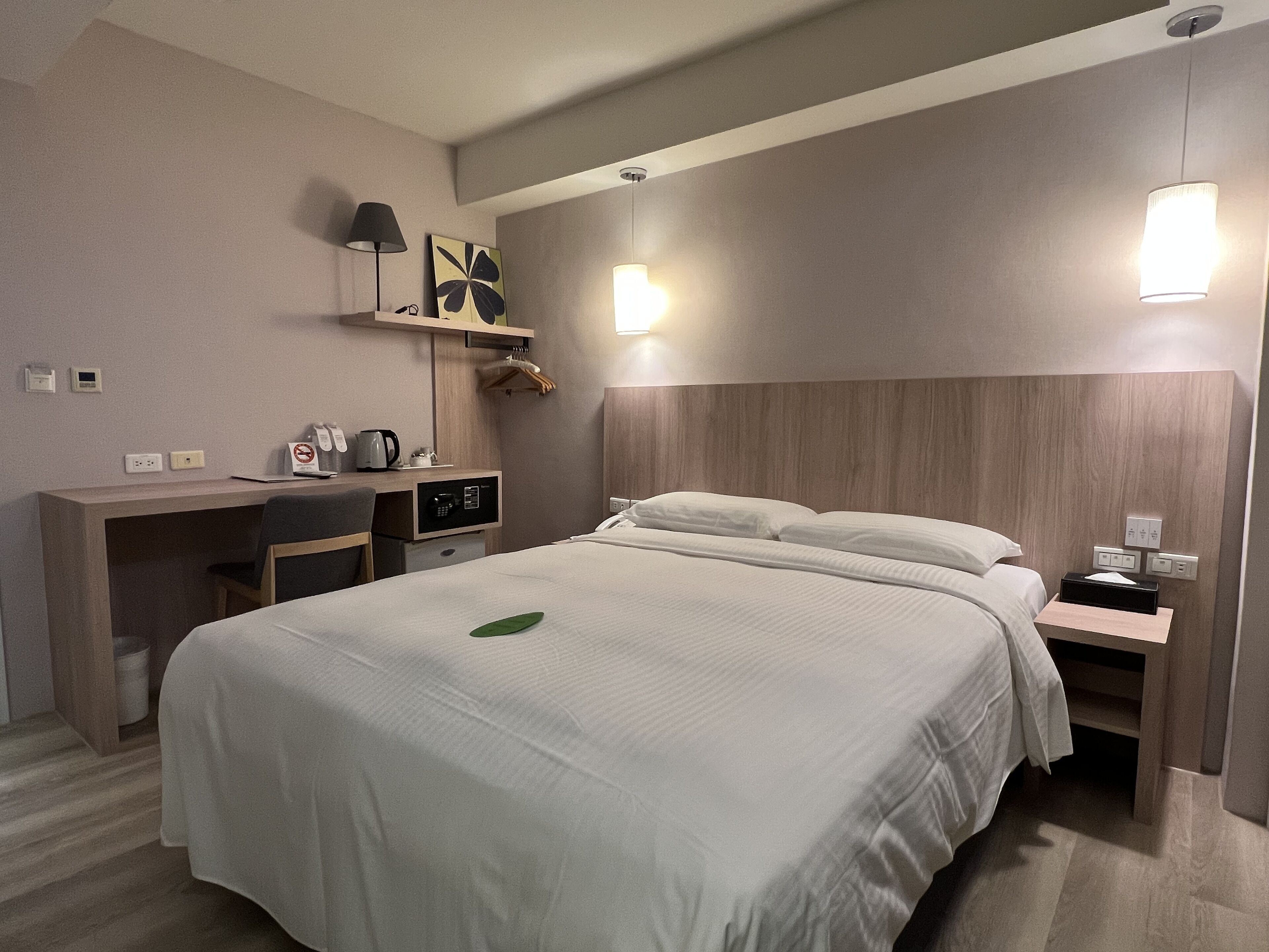 Ein Hotelzimmer mit Bett, Nachttisch, Schreibtisch, Stuhl und einem an der Wand befestigten Regal.