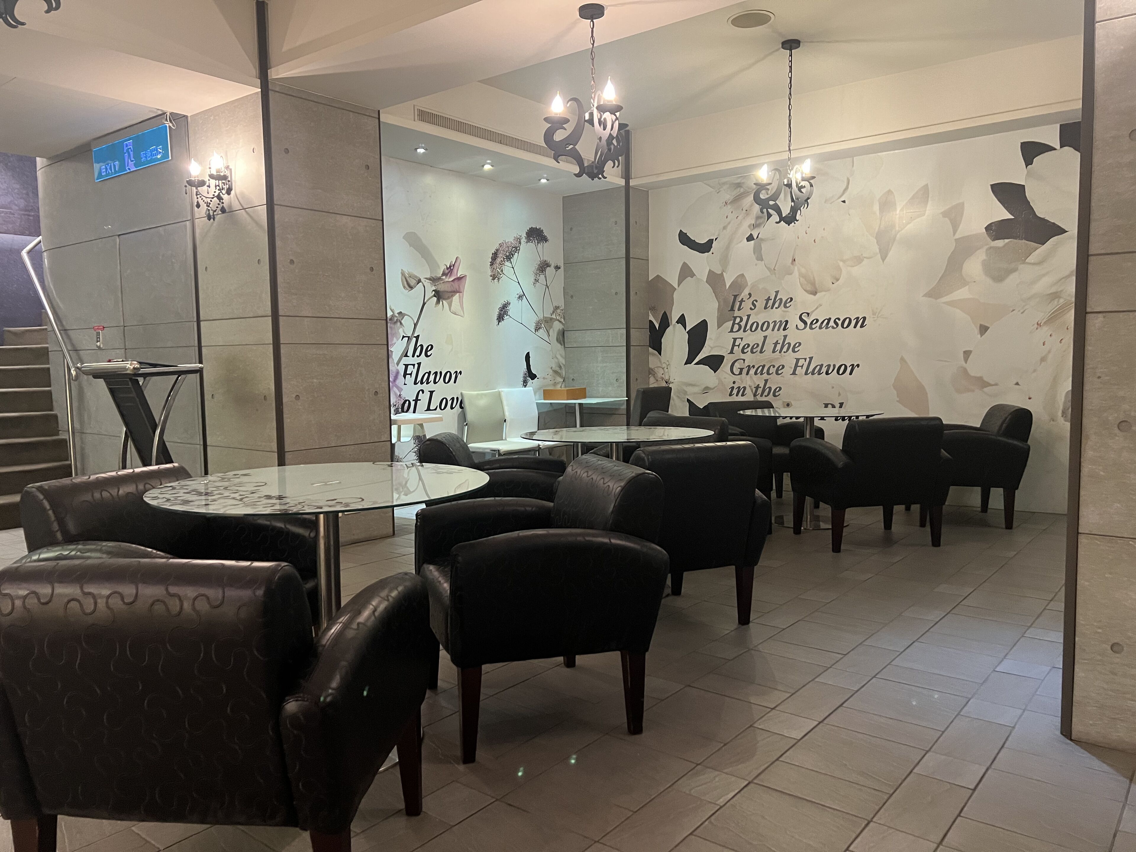 A restaurant interior with round tables, black leather chairs, and a wall with floral artwork.