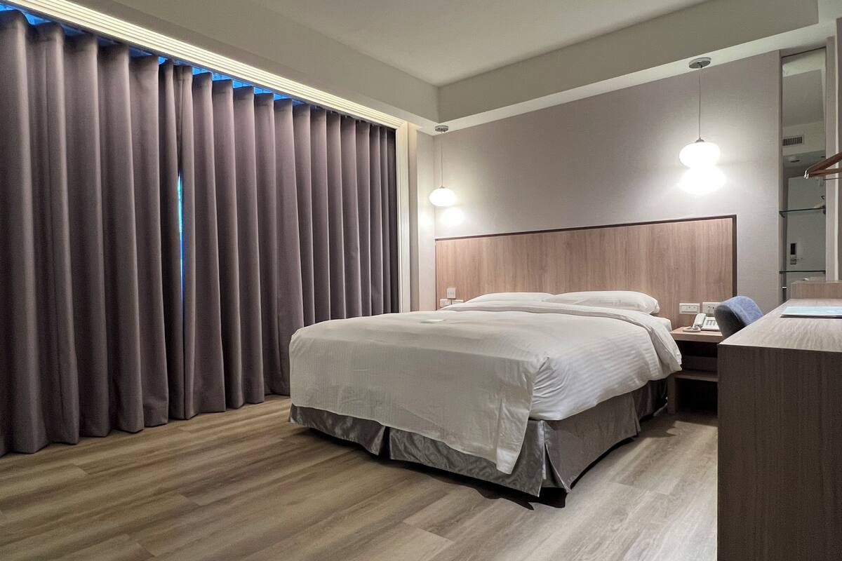Une chambre d’hôtel avec un grand lit, un bureau avec une chaise, une table de chevet et un miroir.