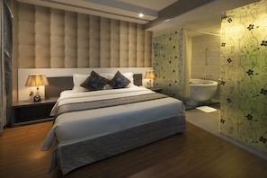 A modern hotel room with a large bed, two bedside tables with lamps, a bathroom with a bathtub, and floral wallpaper.