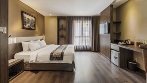 Una habitación de hotel moderna con una cama grande, una kitchenette pequeña, un escritorio y un ventanal con cortinas.