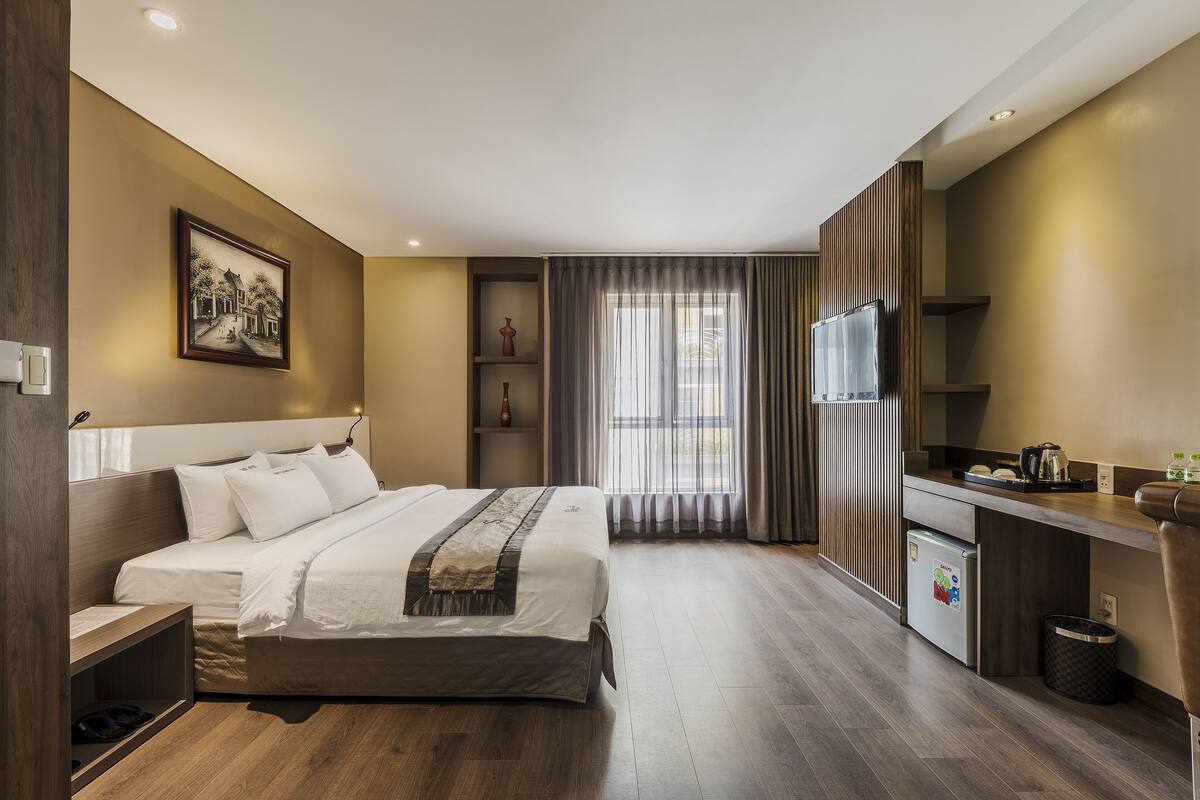 A modern hotel room with a large bed, a small kitchenette, a desk, and a window with curtains.
